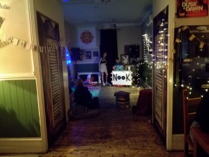 photo of a deceptivly empty bar. Fairy lights on the walls and blankets and pillows on the floor. a dj decks in the backround 