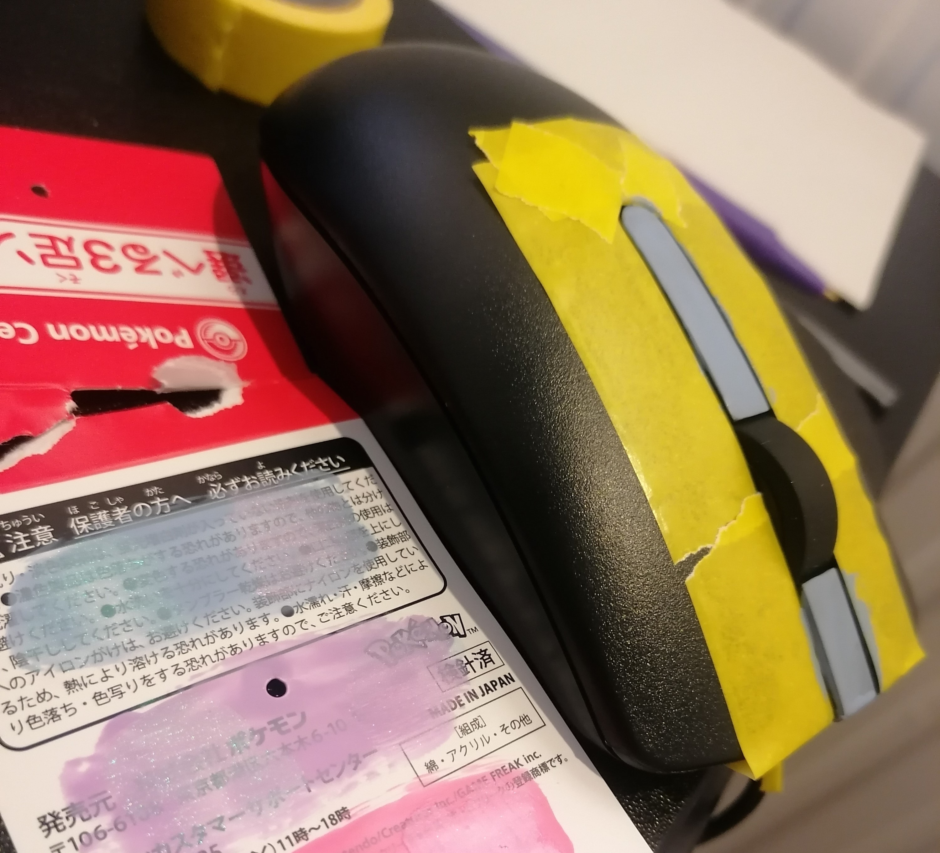 Black mouse with yellow tape over the buttons. Pink and blue nail varnish is swatched on a bit of card.